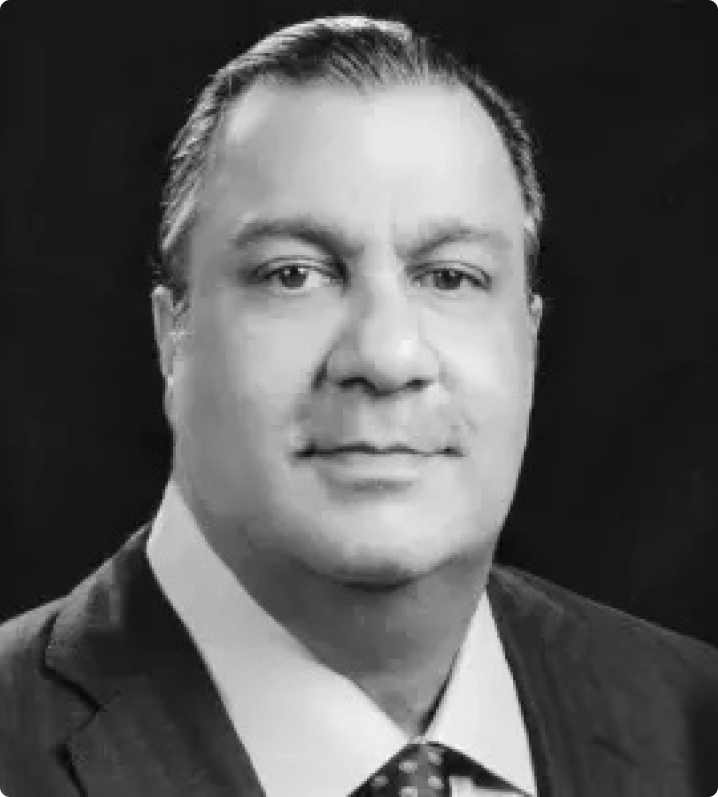 Black-and-white portrait of a middle-aged man with dark, slicked-back hair, wearing a suit and tie, looking directly at the camera with a neutral expression against a dark background.